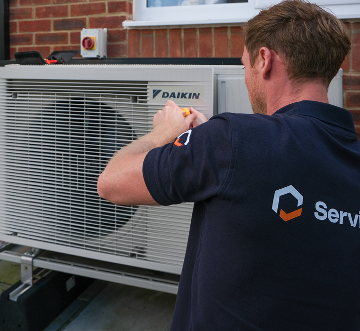 Engineer servicing a Daikin air source heat pump outside a brick house