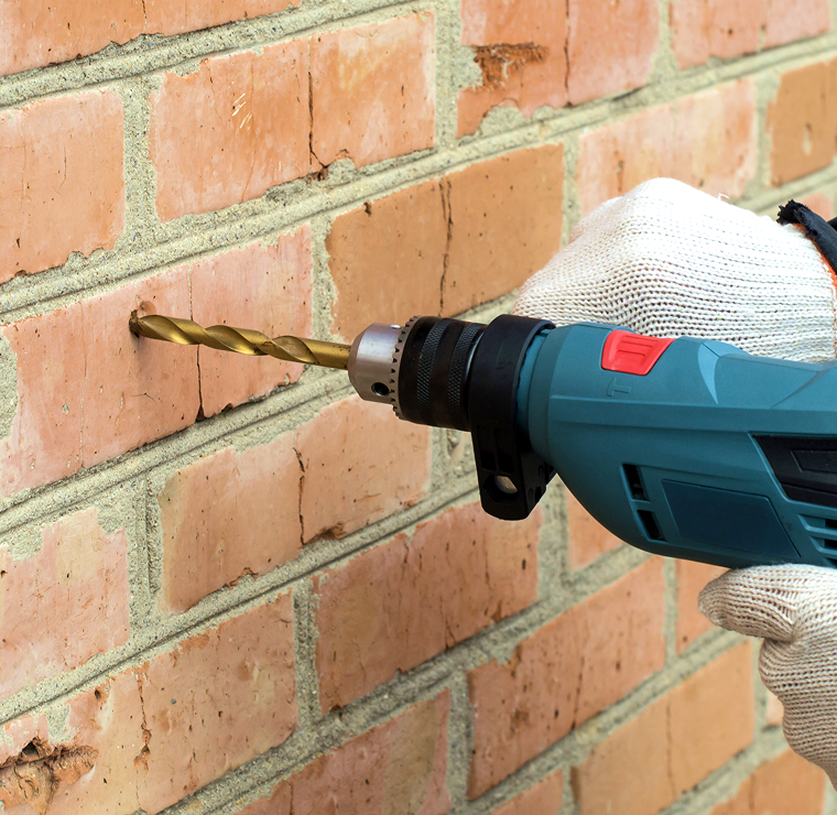 Gloved hand drilling into a brick wall for cavity wall insulation