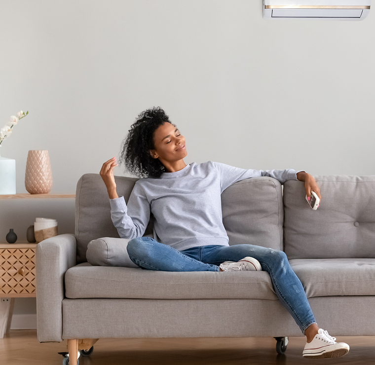 Woman relaxing on a sofa with a remote control beneath a wall-mounted air conditioning unit