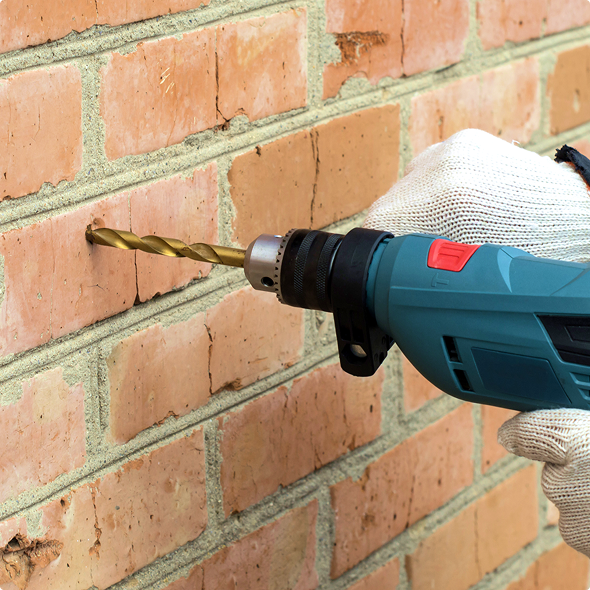 Gloved hand drilling a hole in a brick wall